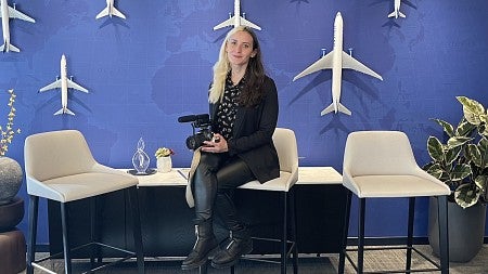 woman sitting on a stool holding a camera with a wall covered in airplanes behind her