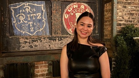 woman smiling at the camera with a brick wall and vintage signs behind her