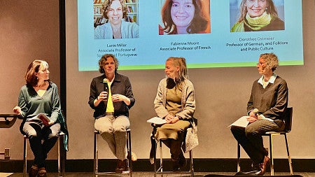 four female faculty members on a stage for a panel discussion with a screen behind them