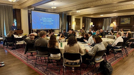 people meeting in a room sitting at tables looking at a presentation screen