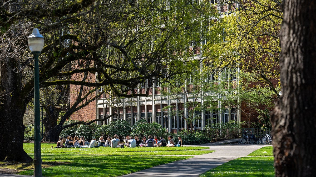 uo students sitting outside on grass in a circle in front of campus building PLC