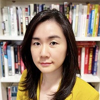 A portrait of Jungmin Kwon, with a bookcase behind her.